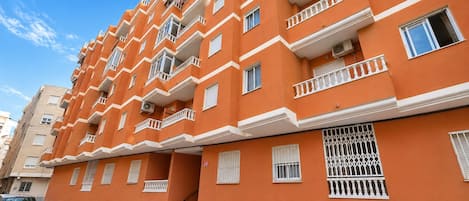 A multi-story orange building with balconies, a staircase, and a gated entrance.