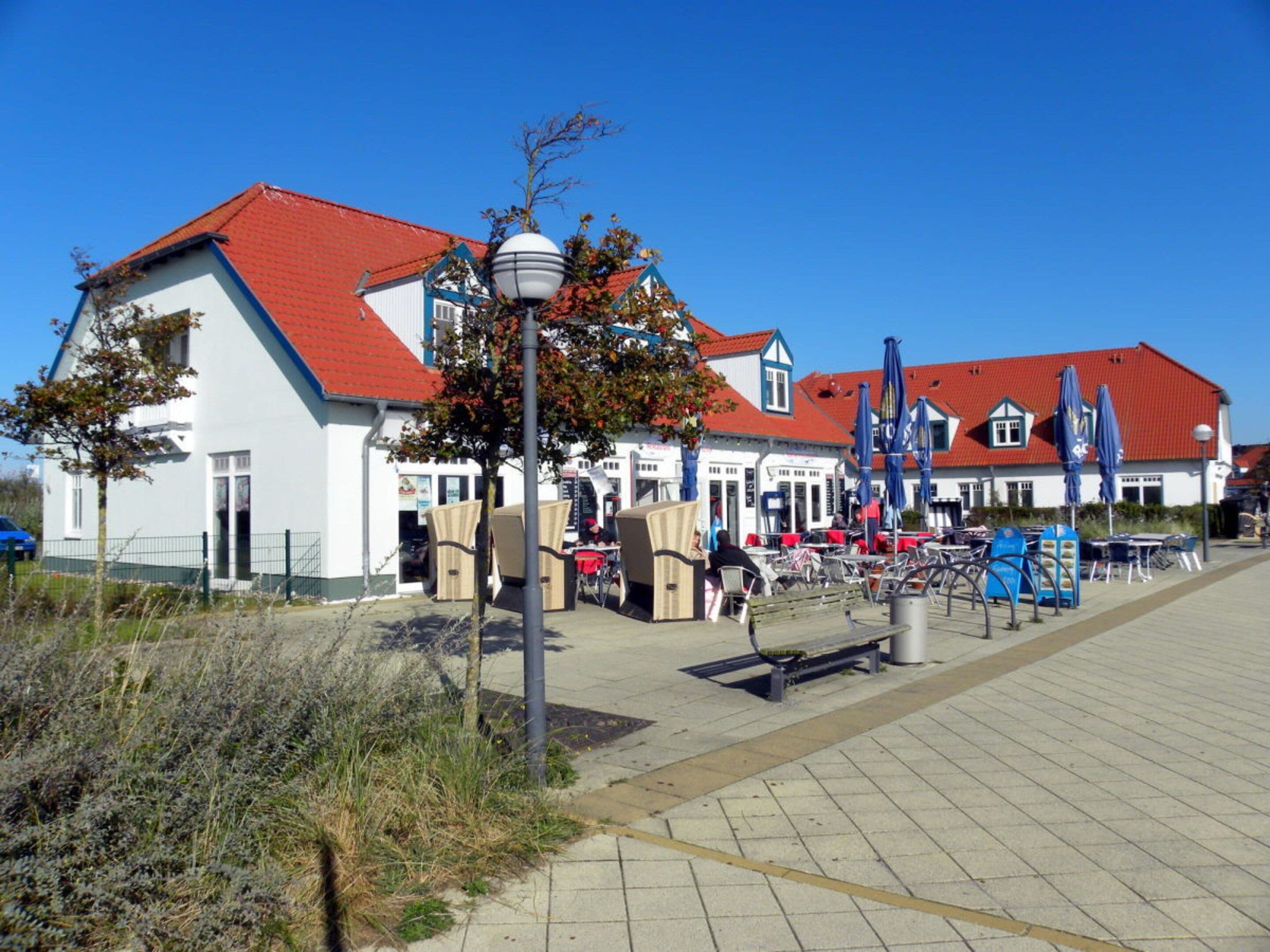 A coastal building with a red roof, outdoor seating, and a paved walkway.