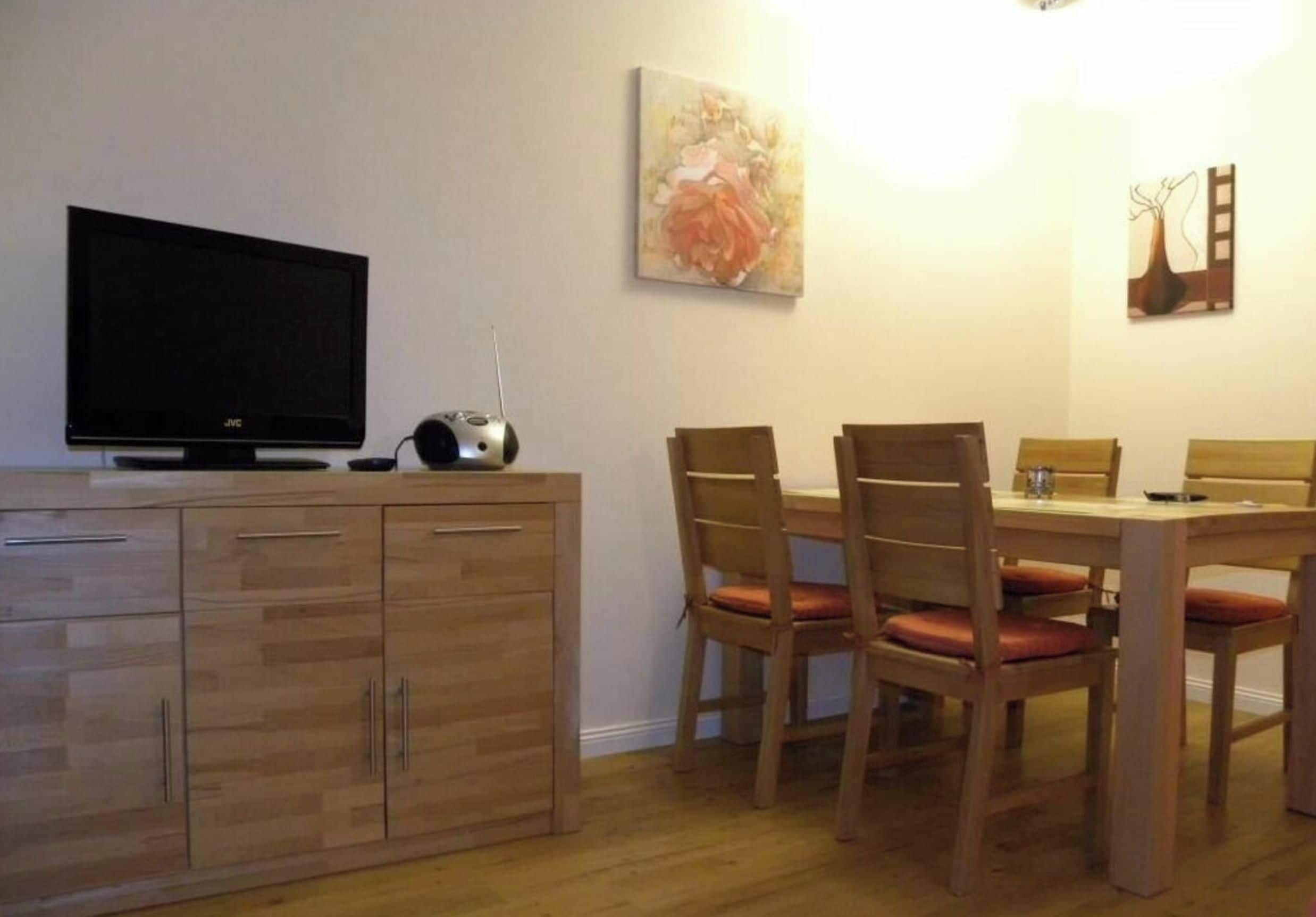 Un comedor con una mesa y sillas de madera, un televisor sobre un mueble y un cuadro en la pared.