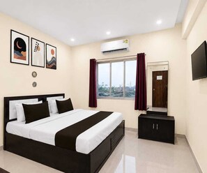 A hotel room with a bed, a wardrobe, a window with curtains, an air conditioning unit, and a flat-screen TV mounted on the wall. - Deluxe RIO Patna (Patna)