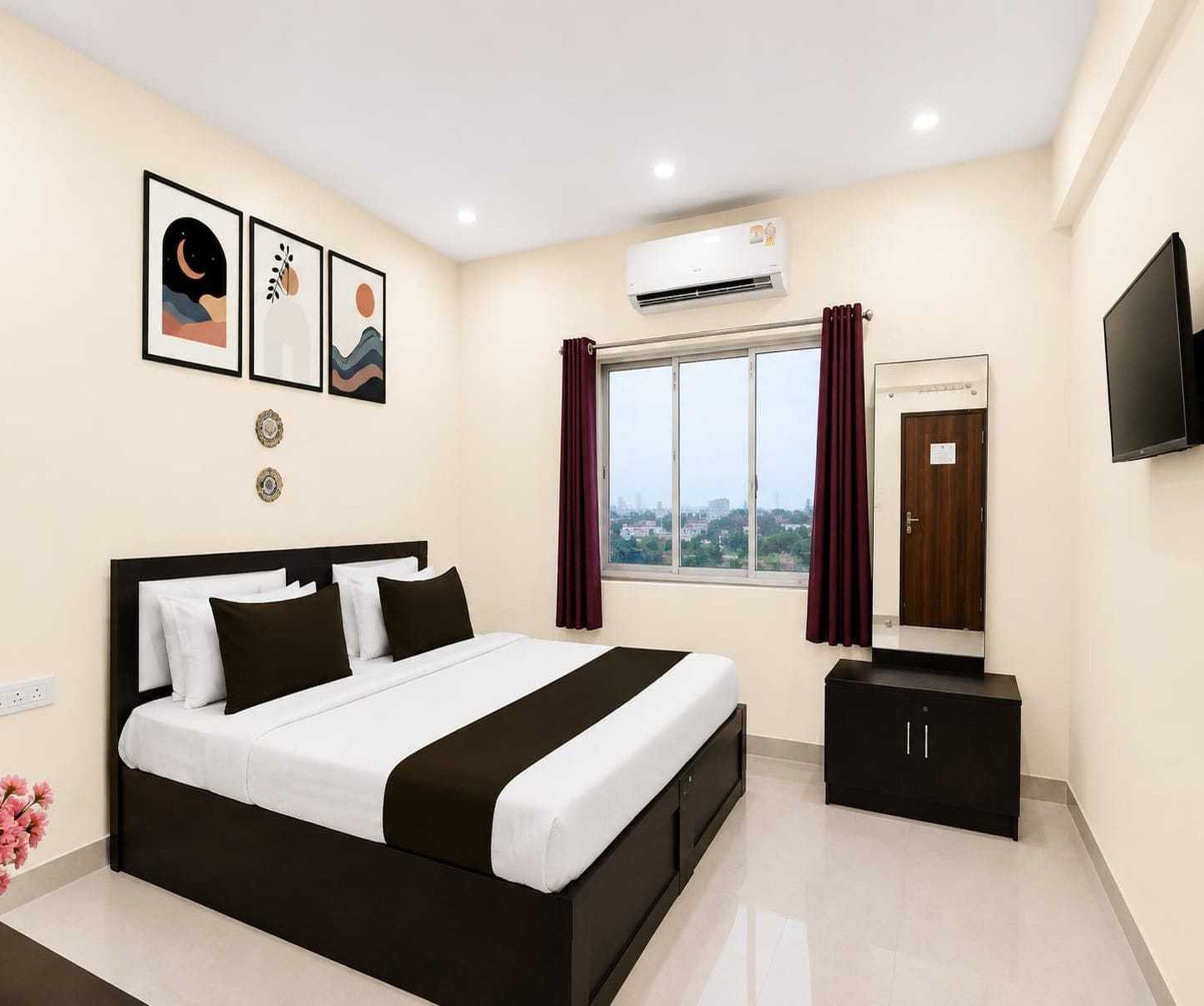 Una habitación de hotel con cama, televisión, ventana con cortinas y una obra de arte en la pared.