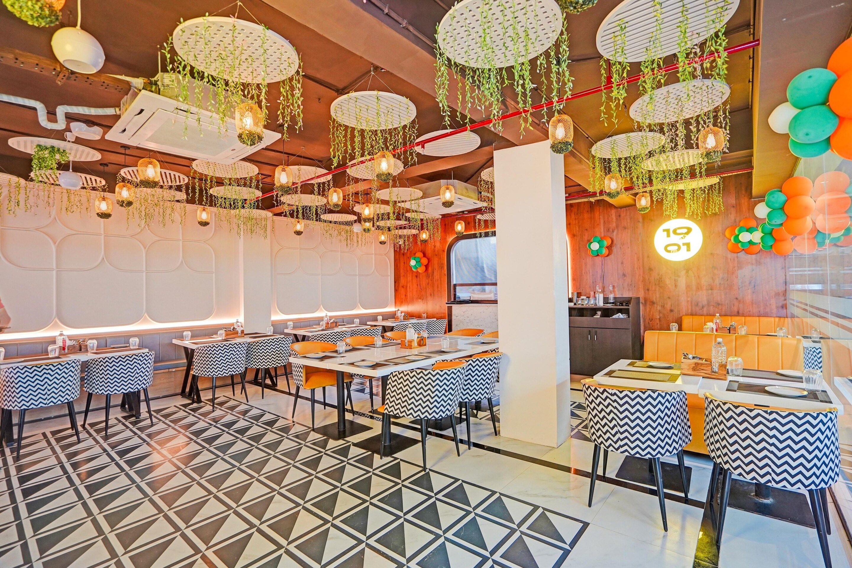 A restaurant interior with multiple tables, chairs, hanging plants, and a patterned floor.
