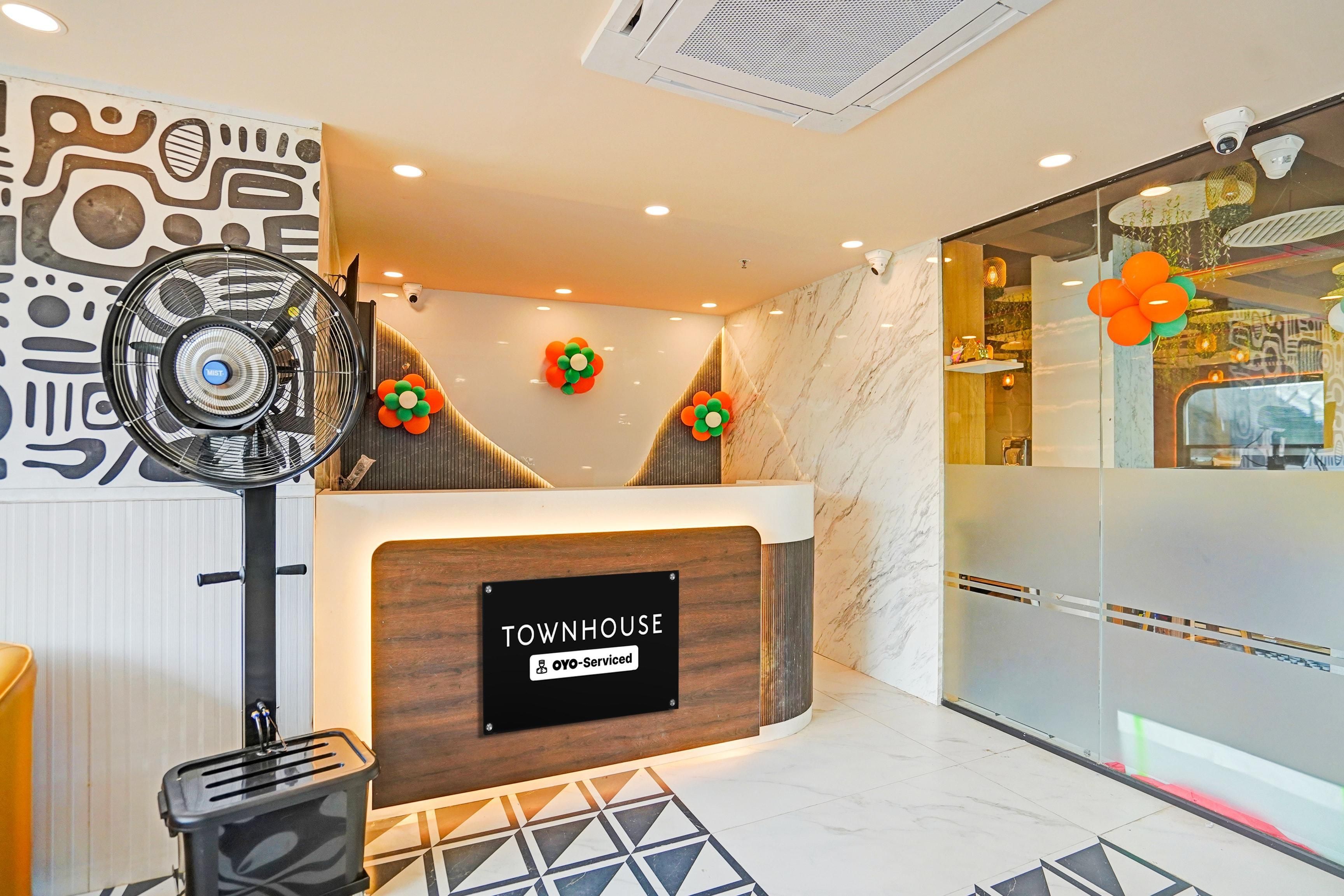 A reception desk with a sign indicating it is serviced by OYO, a modern interior with a fan, a toaster, and a patterned floor.