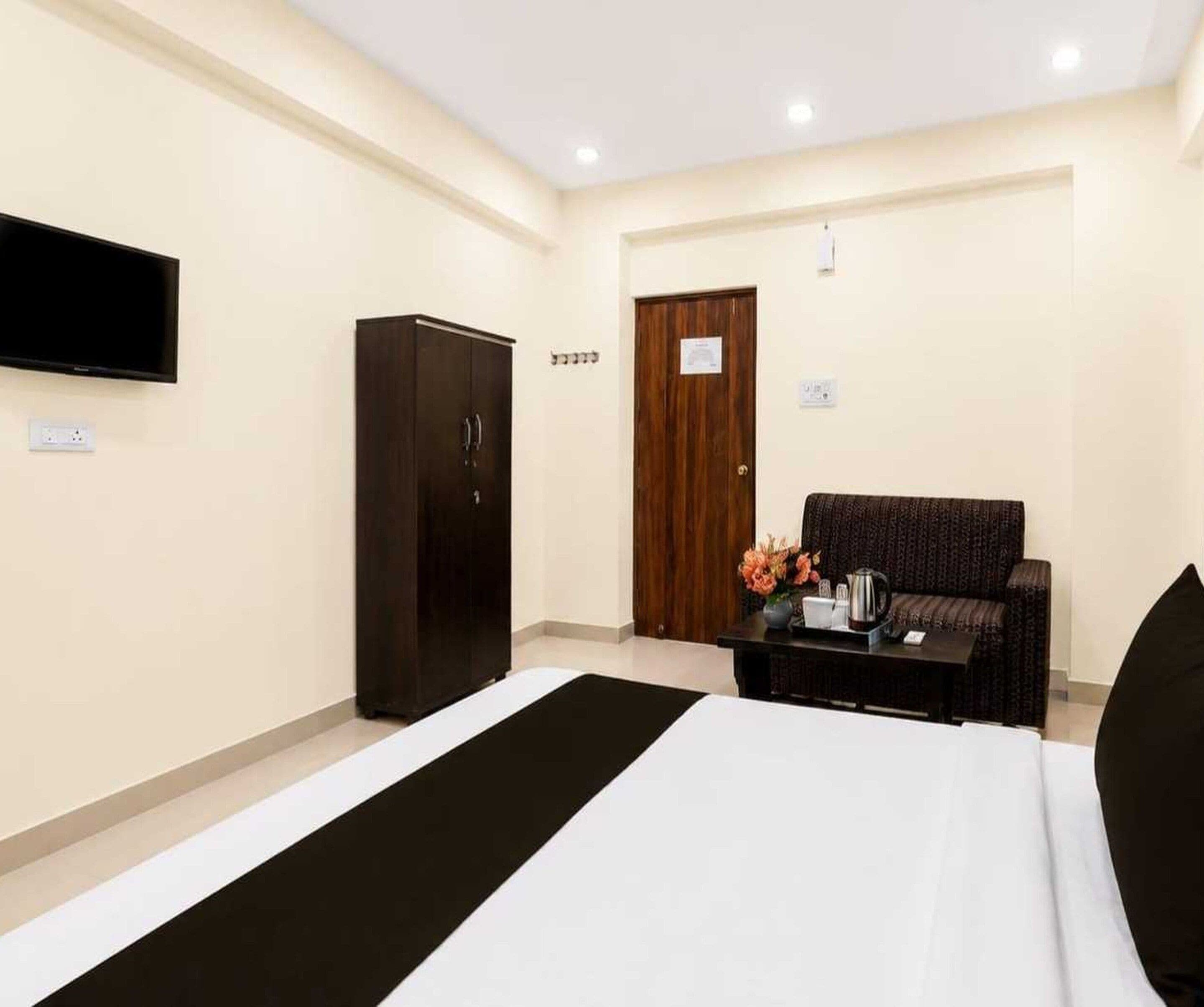 A hotel room with a bed, a wardrobe, a television, and a seating area with a table and flowers.