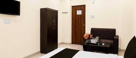 A hotel room with a bed, a wardrobe, a television, and a seating area with a table and flowers.