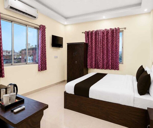 A hotel room with a bed, a TV, a wardrobe, a desk with a kettle, and curtains.