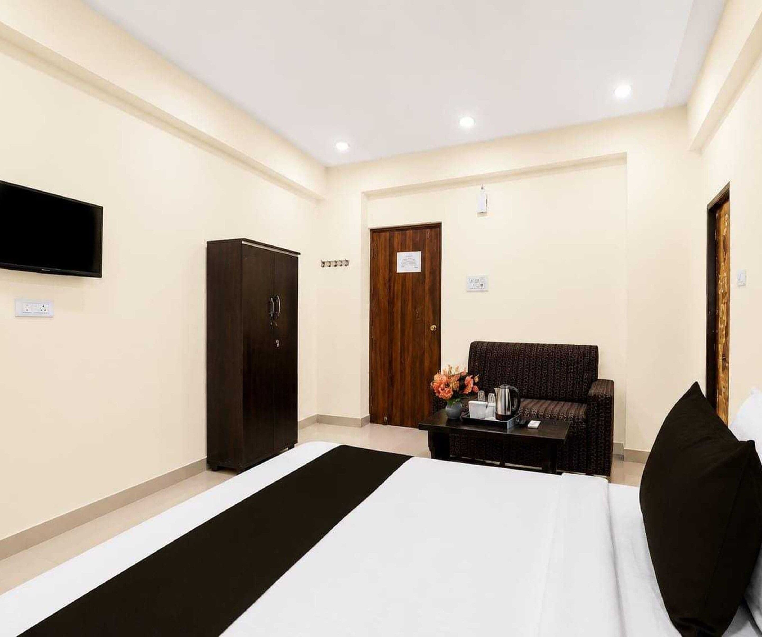 Habitación de hotel con cama, armario, sofá, televisión y mesa de centro con flores.