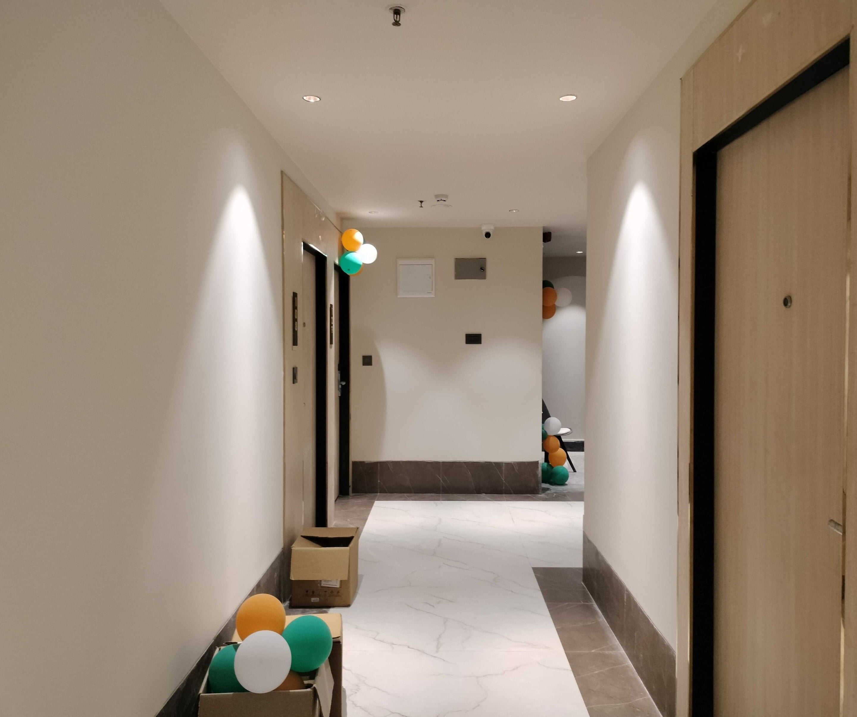 A hallway with a marble floor, doors on both sides, and a box with balloons at the end.