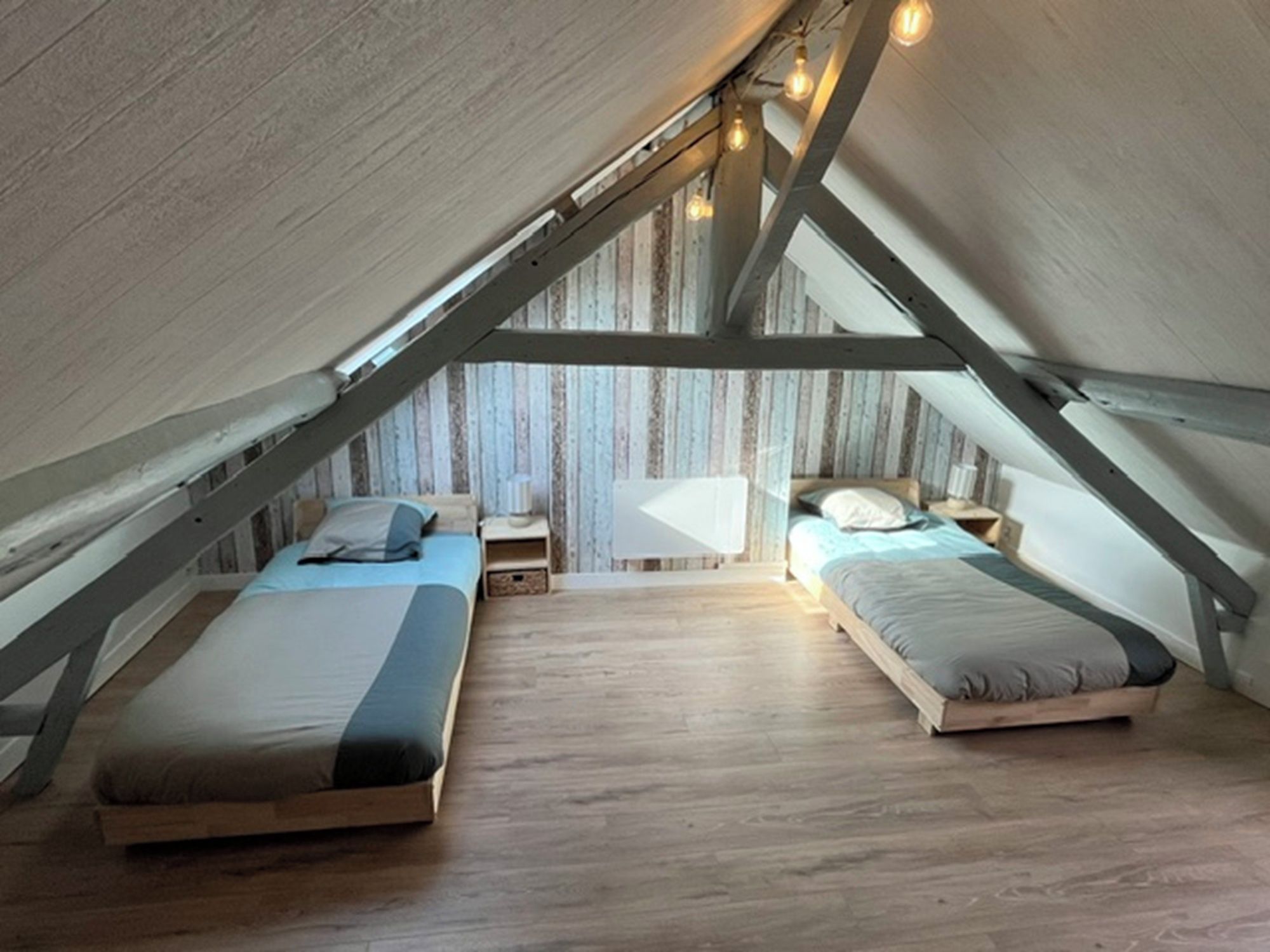 A loft bedroom with two beds, wooden flooring, and exposed wooden beams.