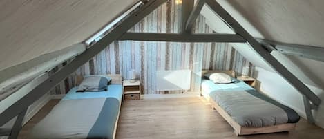 A loft bedroom with two beds, wooden flooring, and exposed wooden beams.