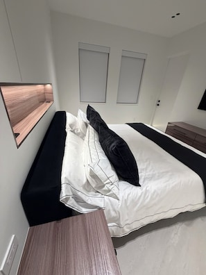 A modern hotel room with a bed, a bedside table, and a wall-mounted TV. - Designer River District Townhouse (Fort Myers)