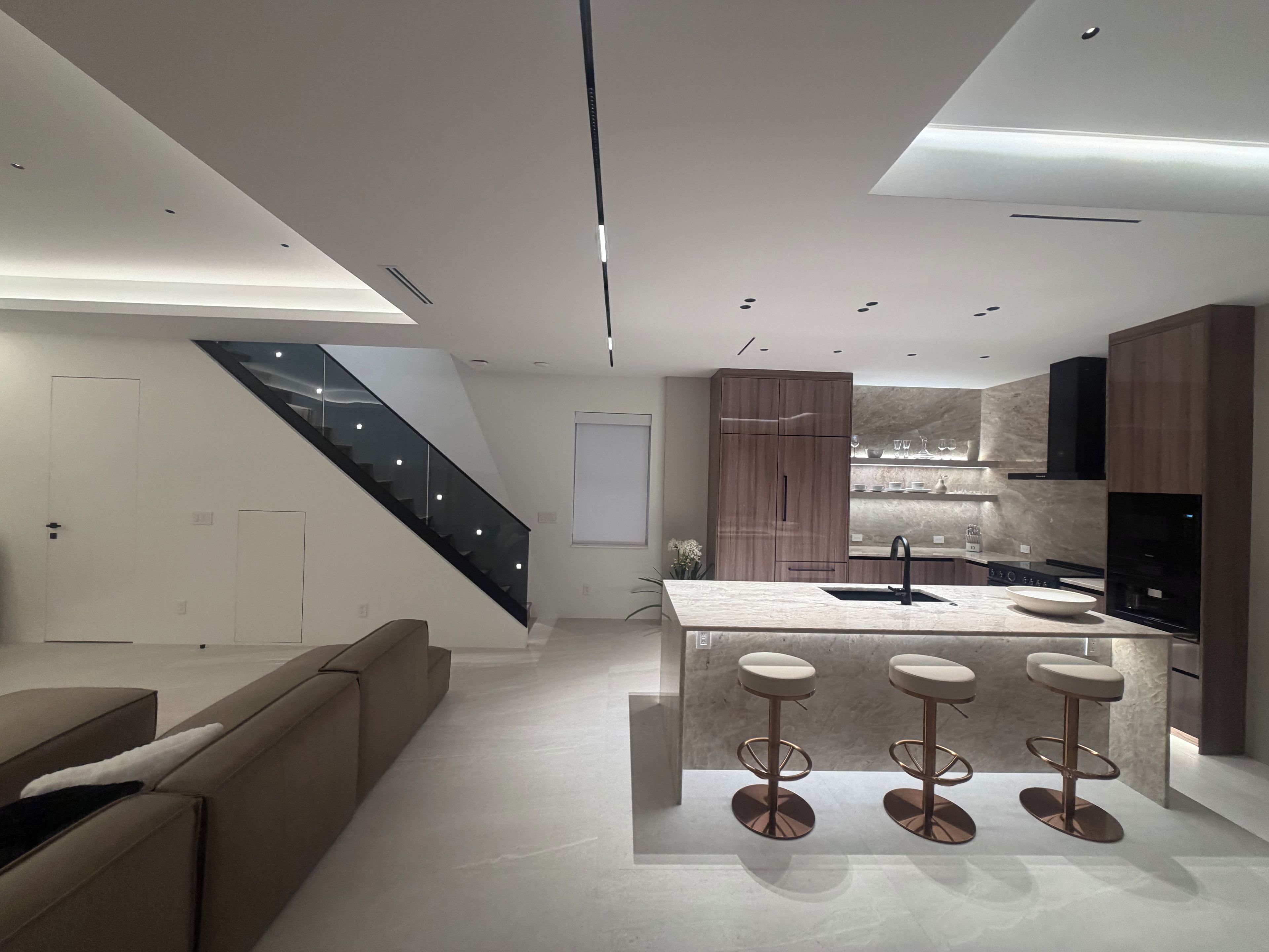 A modern kitchen with a central island, bar stools, and a staircase.