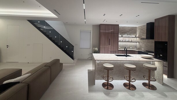 Una cucina moderna con isola centrale, sgabelli da bar e una scala.
