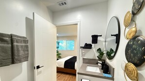 A modern bathroom with a shower, a toilet, a sink, and a mirror. There is a towel rack with towels and a potted plant on the counter. - West Adams 4 S Redondo (Los Angeles)