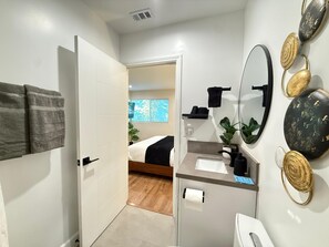 Ein modernes Badezimmer mit Dusche, Toilette, Waschbecken und Spiegel. Ein Handtuchhalter mit Handtüchern und ein Topf mit einer Pflanze befinden sich auf der Ablagefläche.