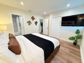 Een slaapkamer met een bed, nachtkastje, lamp, kamerplant en uitzicht op een balkon.