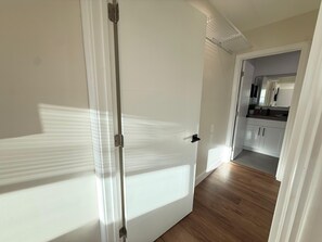 A hallway with a white door, a kitchen area with cabinets and a countertop, and a ceiling with a light fixture.