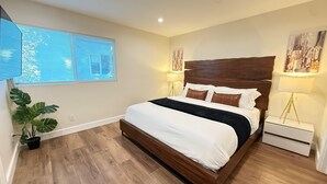 A bedroom with a wooden bed, two bedside lamps, a potted plant, and a cityscape painting on the wall. - West Adams 4 S Redondo (Los Angeles)