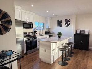 A modern kitchen with white cabinets, a central island with bar stools, a microwave, a stove, and a sink.