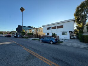 A residential street with houses, a blue car parked on the side, and a clear sky.