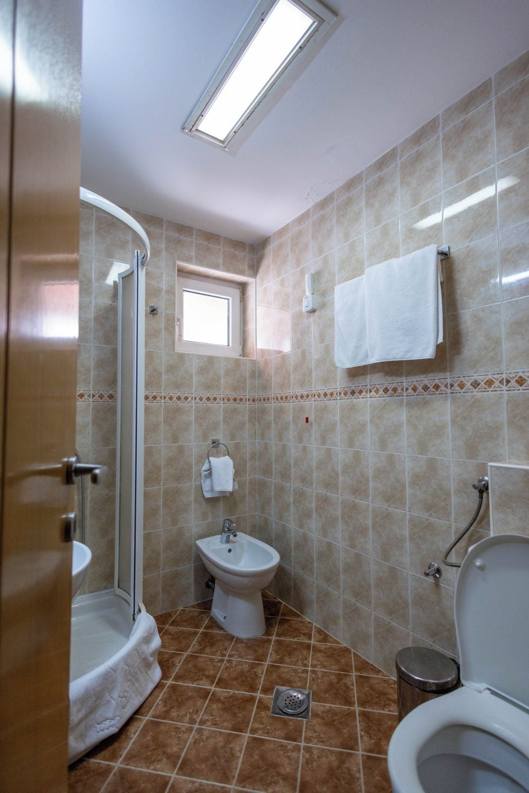 A bathroom with a shower, bidet, toilet, and a small window.