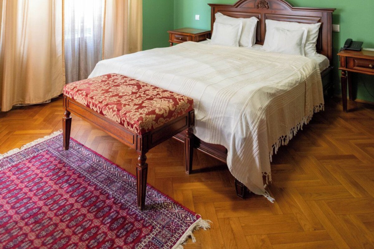 A bedroom with a wooden bed, a red and white patterned bench, green walls, and a wooden floor.