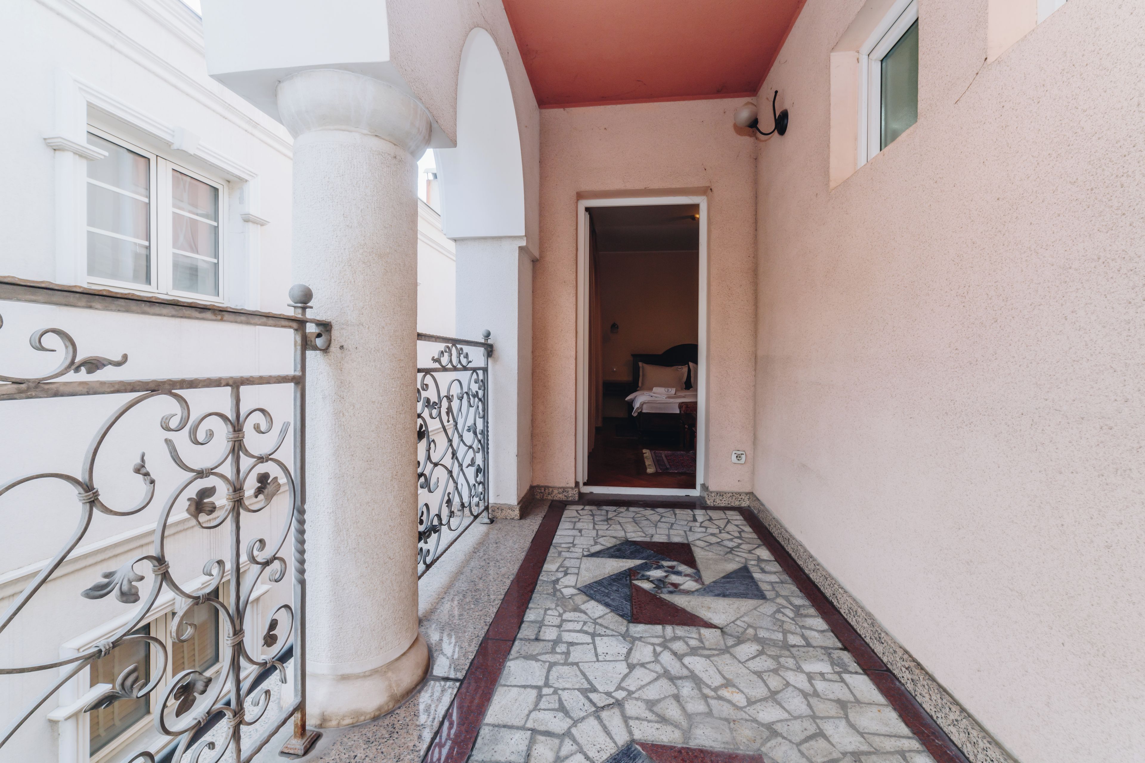 A corridor with a tiled floor, a metal railing, and a doorway leading to a room with a bed.