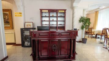 A reception desk with a wooden finish, a reception area with a glass partition, and a dining area with chairs and a table.