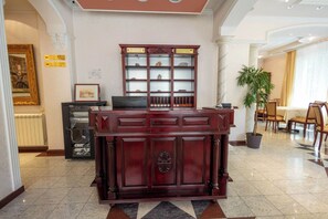 A reception desk with a wooden finish, a reception area with a glass partition, and a dining area with chairs and a table. - Vila Andjelika (Kragujevac)