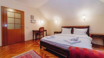 A hotel room with a wooden bed, a desk, a chair, and a red patterned rug.