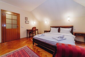 A hotel room with a wooden bed, a desk, a chair, and a red patterned rug. - Vila Andjelika (Kragujevac)