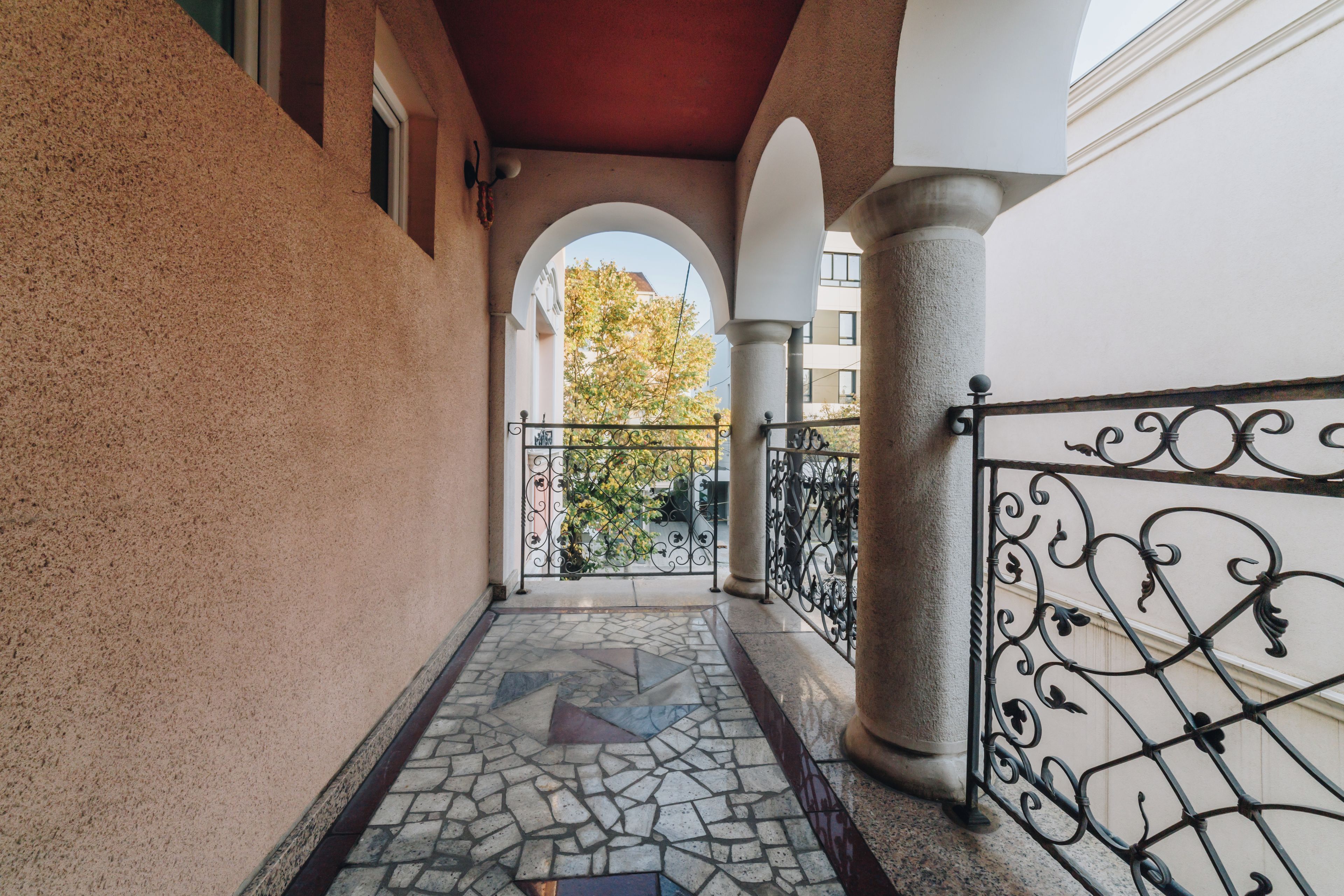A corridor with a tiled floor, a wrought iron gate, and a view of a tree through an archway.