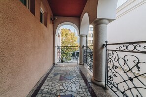A corridor with a tiled floor, a wrought iron gate, and a view of a tree through an archway.