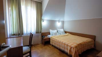 A hotel room with a bed, bedside table, chair, and a window with curtains.