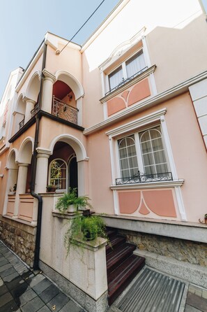 A building with a pink facade, multiple windows with white frames, and a balcony with ornate metal railings.