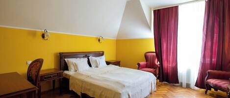 A hotel room with a bed, a desk, a chair, and a window with curtains.
