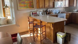 A kitchen with wooden cabinets, a central island with stools, a microwave, and a stove. - Two Bedroom Townhome With Trail Access (Bozeman)