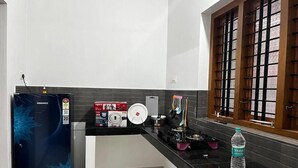A modern kitchen with a black countertop, a refrigerator, a stove, and a window with a grid pattern. - Rivera Home | Lake View Homestay in Kadalundi (Balathiruthi)
