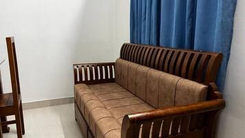 Ein Holzsofa mit gepolstertem Sitz und Rückenlehne, platziert vor einer Wand mit einem blauen Vorhang.