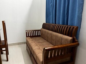 Un sofá de madera con asiento y respaldo acolchados, colocado frente a una pared con cortina azul.