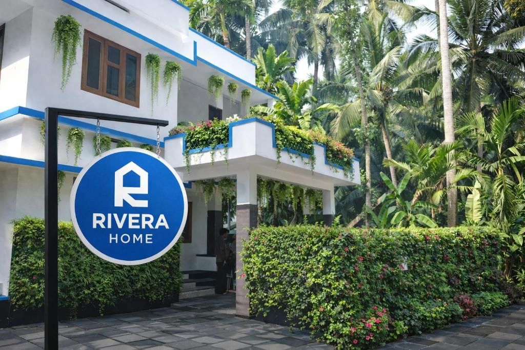 A hotel entrance with a sign reading 'RIVERA HOME,' surrounded by lush greenery and palm trees.