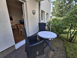 Eine Terrassesituation mit Korbstühlen und einem Tisch, einer Tür zu einem Innenbereich und einer kleinen Gartenanlage.