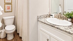 Un baño con inodoro blanco, lavamanos con encimera de granito, espejo y cortina de ducha.