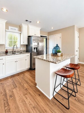 A kitchen with white cabinets, a stainless steel refrigerator, a built-in island with bar stools, and wooden flooring.