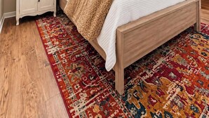 Un dormitorio con cama, mesitas de noche, ventilador de techo y alfombra estampada.