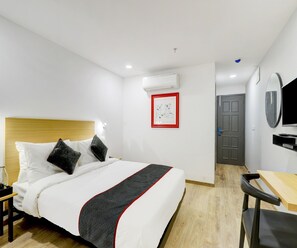 A hotel room with a bed, a desk, a chair, a television, and a door. - Super Deluxe Room Hotel Rajyash Rise (Ahmedabad)