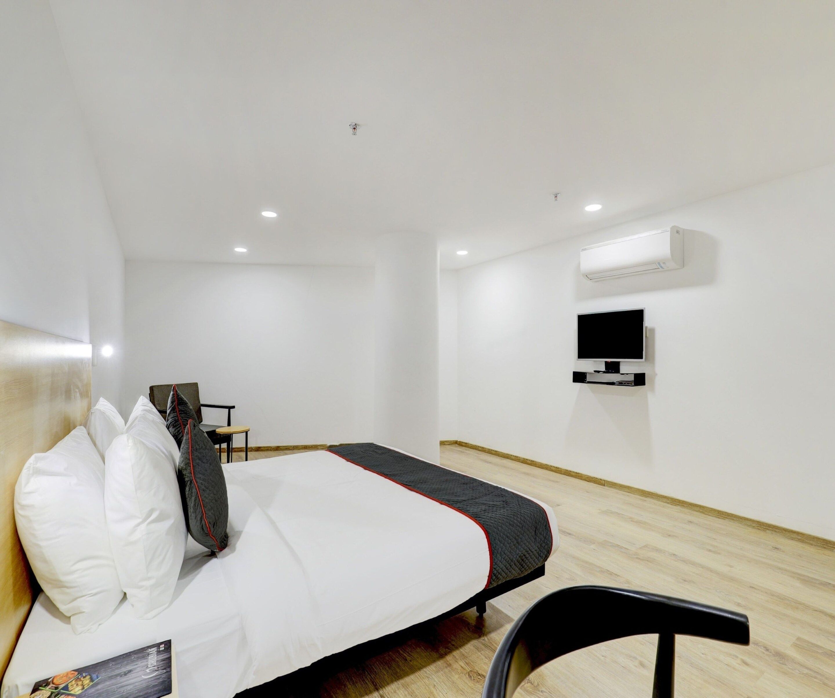 Una habitación de hotel con cama, una silla, televisor y aire acondicionado.