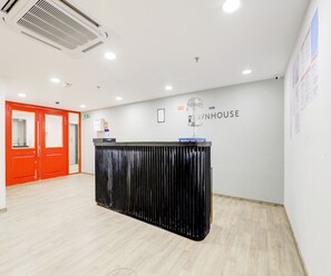 A reception desk with a black surface and a glass object on top, a red door, and a wall with the text 'OYO WHOUSE'. - Super Deluxe Room Hotel Rajyash Rise (Ahmedabad)