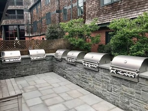 A patio with a stone wall and multiple barbecue grills. - Deluxe 2BR at Wyndham Long Wharf Resort -walk to downtown - 2.3 miles from Beach (Newport)