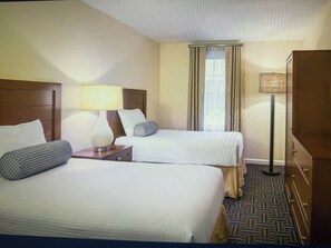Una camera d'albergo con due letti, un comodino con una lampada, una cassettiera e una finestra con tende.